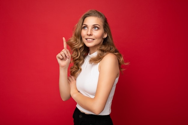 Foto van een aantrekkelijke, positieve jonge vrouw die met haar vingers omhoog wijst naar copyspace en reclamepromo presenteert met