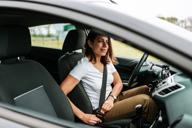 Foto van een bedrijfsvrouwenzitting in een auto die op haar veiligheidsgordel zet.