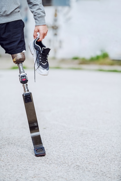 Foto van een blanke gehandicapte sportieve man uitgesneden die buiten met sneaker in de hand staat.
