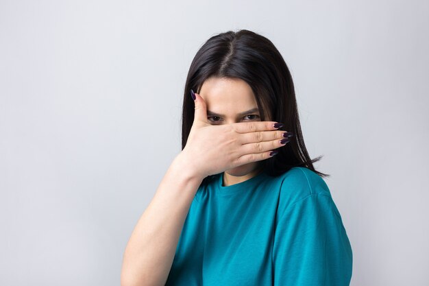 Foto van een brunette tienermeisje dat haar gezicht bedekt met handen en door haar vingers gluurt.