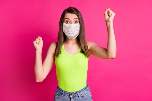 Foto van een charmant jong meisje dat vuisten opheft en een roze gezichtsmasker draagt, een geïsoleerde levendige roze kleurachtergrond