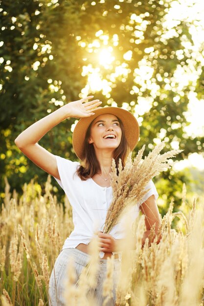 Foto van een charmante blanke vrouw met een strohoed die op een zomerdag op een tarweveld rust