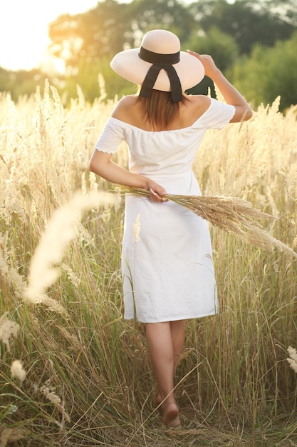 Foto van een charmante blanke vrouw met een strohoed die op een zomerdag op een tarweveld rust