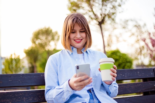 Foto van een charmante, mooie jonge dame die een moderne gadget op een bankje communiceert die buiten glimlacht