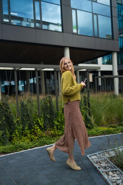 Foto van een coole millennial blonde vrouw buiten in de stad die naar een mobiele telefoon kijkt in de stad in hoge kwaliteit