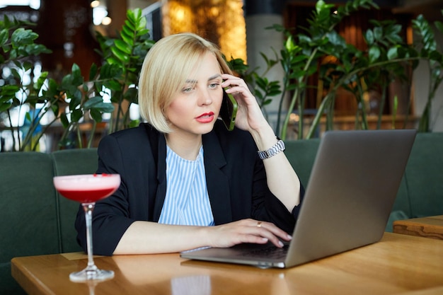 Foto van een geïnspireerd aantrekkelijk model dat op haar laptop schrijft en tijd alleen doorbrengt in een café met een glas cocktail op tafel terwijl ze bezig is met het dragen van een pak