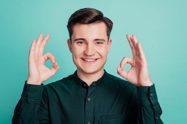 Foto van een gelukkige man die twee ok-teken-vingers toont op een turkooizen achtergrond