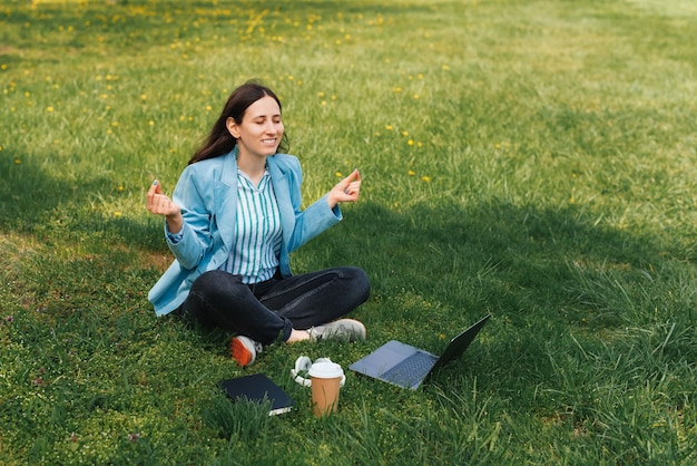 Foto van een gelukkige vrouw in casual zittend op het gras in het park en uitrusten en mediteren