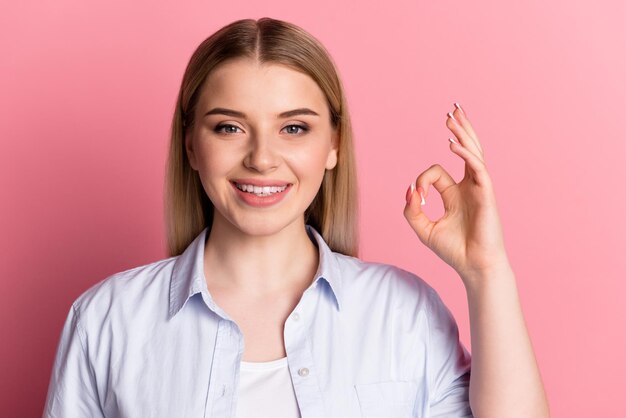 Foto van een jong vrolijk meisje toont vingers okey-symbool beveel promotie aan geïsoleerd over roze kleur achtergrond