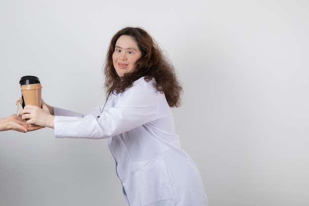 Foto van een jong vrouwenmodel in wit uniform dat een kopje koffie geeft.