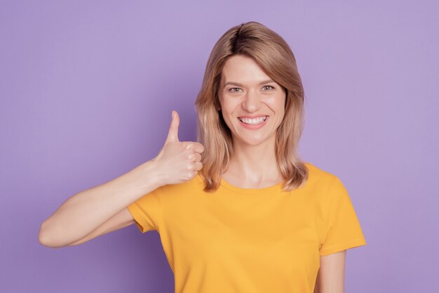 Foto van een jonge, aantrekkelijke vrouw die blij is met een positieve glimlach, duim omhoog als een geïsoleerde violette kleurachtergrond