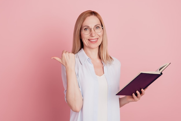 Foto van een jonge aantrekkelijke vrouw, gelukkig positief glimlachpunt, duim lege ruimte suggereert boek geïsoleerd over pastelkleurige achtergrond