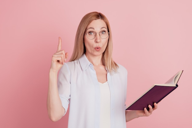 Foto foto van een jonge aantrekkelijke vrouw, gelukkig positief glimlachpuntvinger, heeft een ideeboek geïsoleerd over een pastelkleurige achtergrond