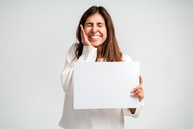 Foto van een jonge, gelukkige positieve vrouw die een leeg reclamebord vasthoudt voor advieskeuze geïsoleerd op een witte achtergrondkleur