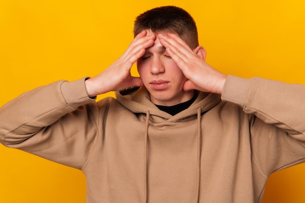 Foto foto van een jonge man die op een gele achtergrond staat en hoofdpijn heeft