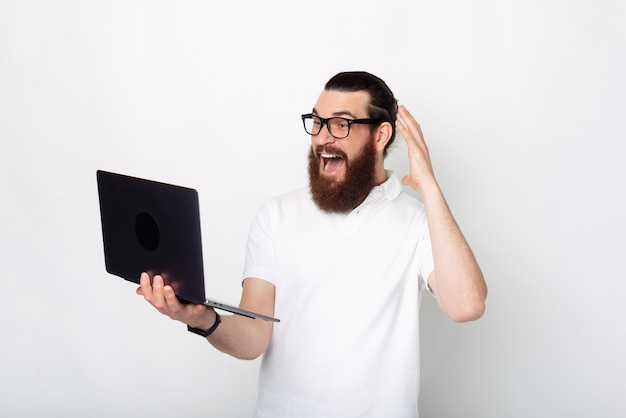 Foto van een jonge man met baard in casual kijken verbaasd op laptop op witte achtergrond