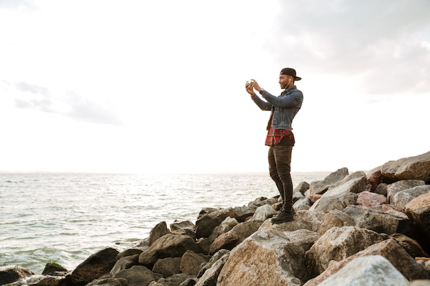 Foto van een jonge man met een pet die op het strand loopt terwijl hij naar muziek luistert met een koptelefoon.