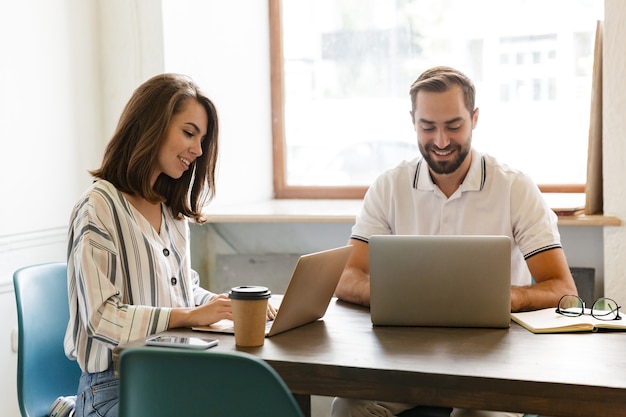 Foto van een jonge optimistische vrolijke positieve paar collega's werken met laptopcomputers binnenshuis op kantoor.