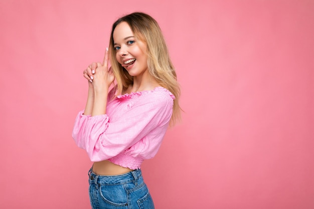 Foto van een jonge positieve, gelukkige, aantrekkelijke blonde vrouw met oprechte emoties die een roze blouse draagt