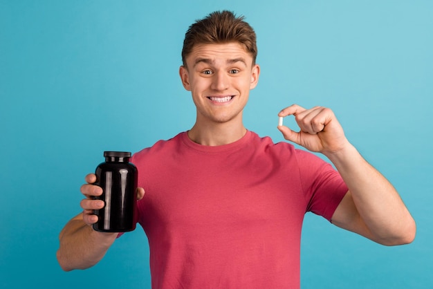 Foto van een jonge vrolijke man die reclame maakt voor medicijnen die medicijnen bevatten, raden aan om geïsoleerd op een blauwe achtergrond te adviseren