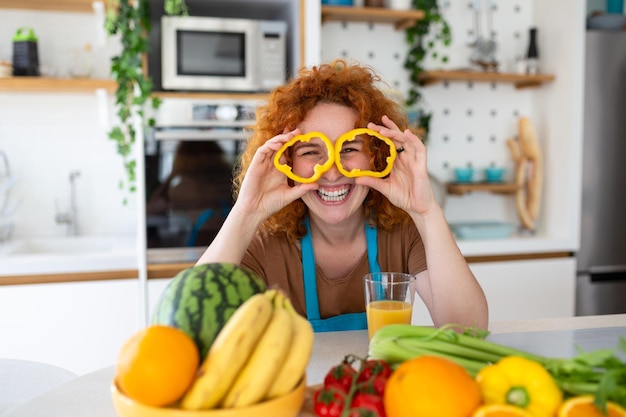 Foto van een jonge vrouw die lacht tijdens het koken van salade met verse groenten in het keukeninterieur thuis