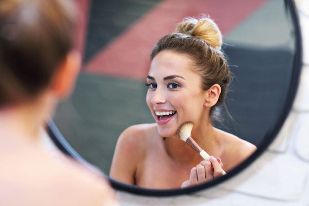 Foto van een jonge vrouw die make-up aanbrengt met borstel in de badkamer