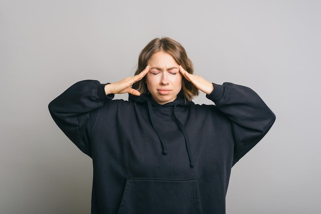 Foto van een jonge vrouw die migraine heeft en over een grijze achtergrond staat