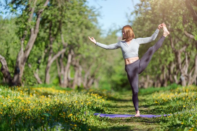 Foto van een jonge vrouw die 's middags op één been staat in yoga in het bos