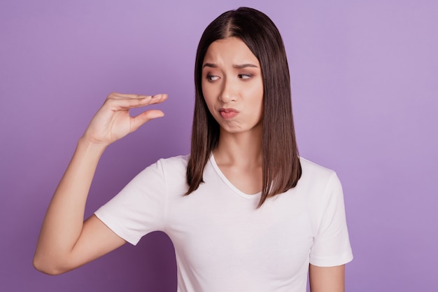Foto van een jonge vrouw, ongelukkig, verdrietig, overstuur, laat de vingers zien, een kleine, kleine maatmaat geïsoleerd over een violetkleurige achtergrond