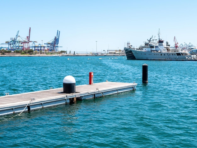 Foto van een kleine pier in de haven met op de achtergrond afgemeerde jachten en schepen