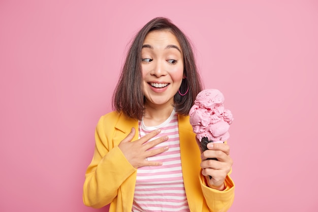 Foto van een knappe jonge aziatische vrouw met donker haar met lekker ijs in een wafelkegel glimlacht graag gekleed in een stijlvolle outfit en wil een heerlijk bevroren zomerdessert eten. geniet ervan.