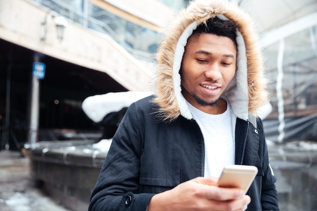 Foto van een knappe jonge man die op straat loopt terwijl hij zijn telefoon gebruikt.