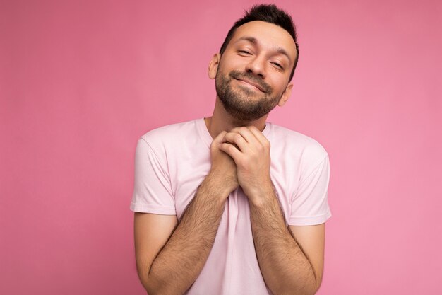 Foto van een knappe, schattige, positieve brunette man in een casual roze t-shirt geïsoleerd op een roze achtergrond