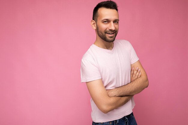 Foto van een knappe zelfverzekerde, positieve brunette man in een casual roze t-shirt geïsoleerd op een roze achtergrond