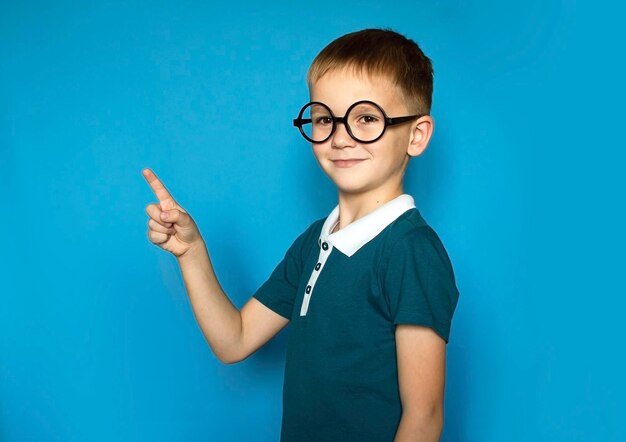 Foto foto van een lachende gelukkige jongen die met zijn vinger wijst naar de plek om te kopiëren gemarkeerd op een eenvoudige achtergrond terug naar school grappige jongen met een bril van de basisschool onderwijs
