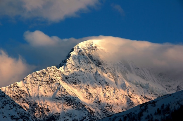 Foto van een met sneeuw bedekte berg met een gletsjer en wolken weggeblazen door de wind