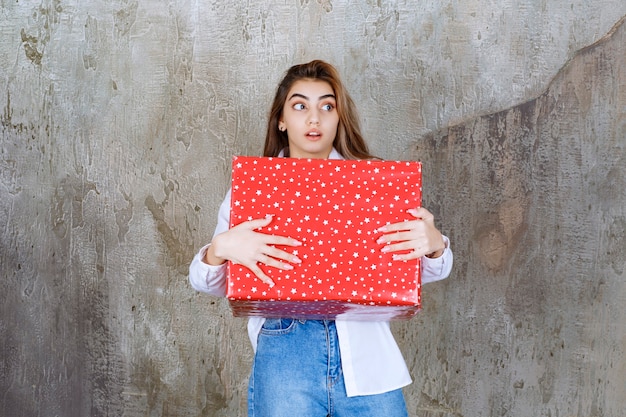 Foto van een mooi meisjesmodel met lang haar dat een groot rood cadeau houdt