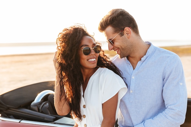 Foto foto van een mooi multi-etnisch stel man en vrouw die samen knuffelen en glimlachen terwijl ze buiten in de auto staan