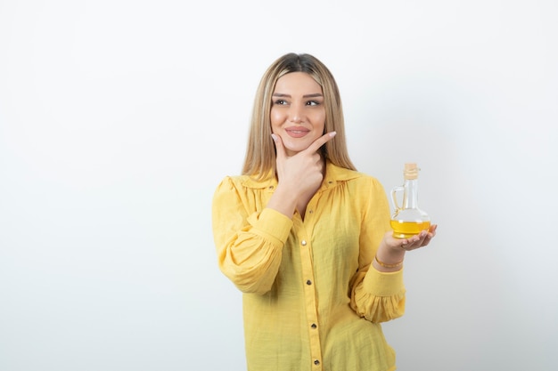 Foto van een mooi vrouwenmodel in geel overhemd met een glasfles olie