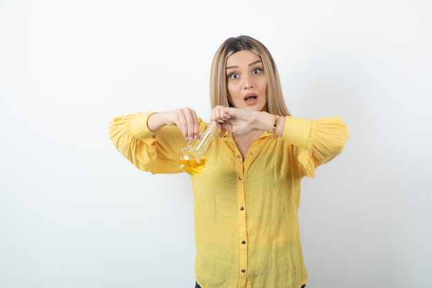 Foto van een mooi vrouwenmodel in geel overhemd met een glasfles olie