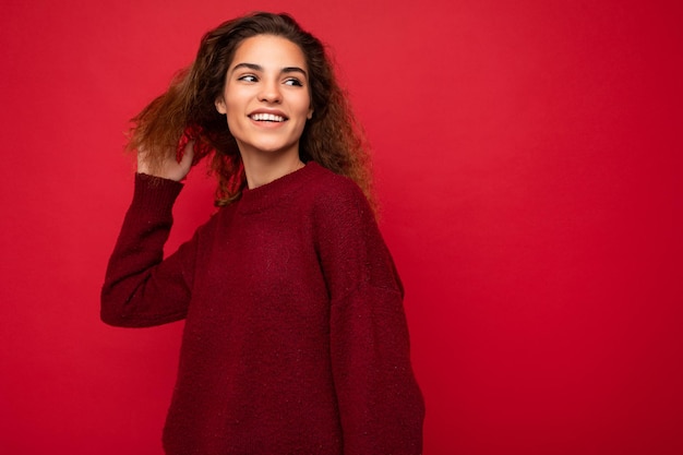 Foto van een mooie, charmante, jonge, brunette, krullende vrouw die een stijlvolle donkerrode trui draagt