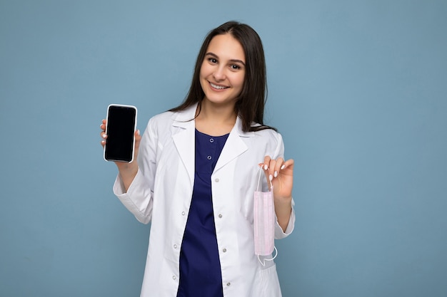 Foto van een mooie glimlachende jonge brunette vrouw die er goed uitziet met een witte medische jas staand