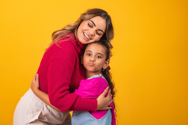 Foto van een mooie jonge mama die haar armen vasthoudt en haar dochtertje knuffelt goed humeur schattig oprecht hartgevoel in de rug jeans t-shirts geïsoleerd met gele kleur achtergrond