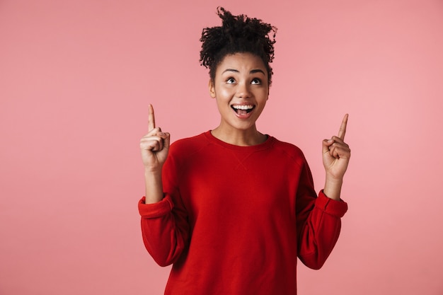 Foto van een mooie jonge opgewonden emotionele schattige gelukkige emotionele Afrikaanse vrouw die zich voordeed over het roze muur wijzen.