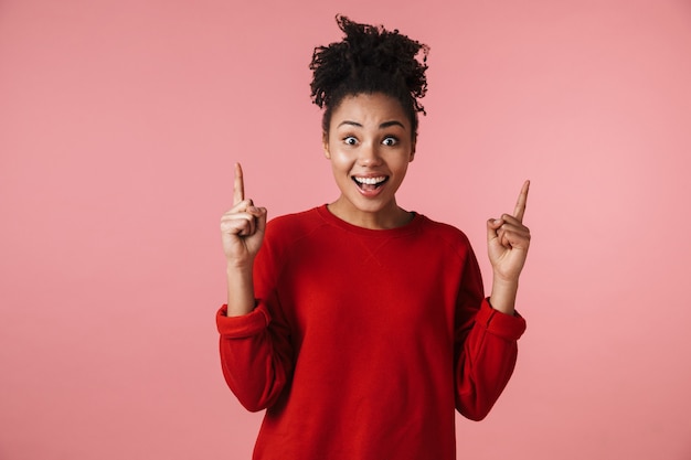 Foto van een mooie jonge opgewonden emotionele schattige gelukkige emotionele Afrikaanse vrouw die zich voordeed over het roze muur wijzen.