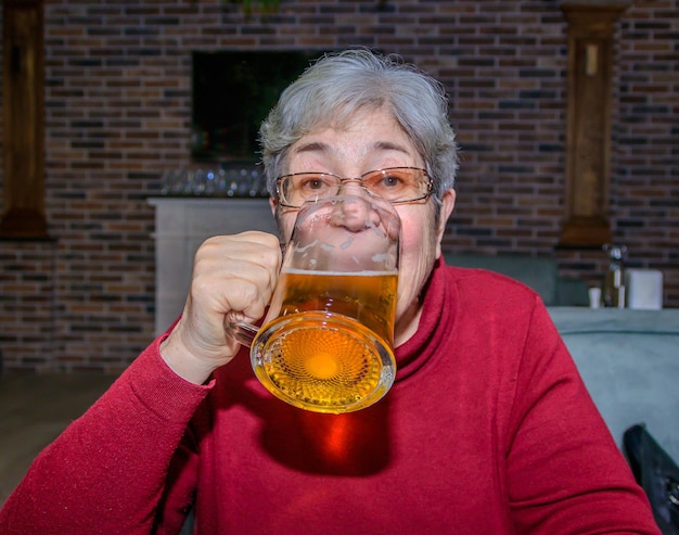 foto van een oudere vrouw die bier drinkt uit een biermug in een bar