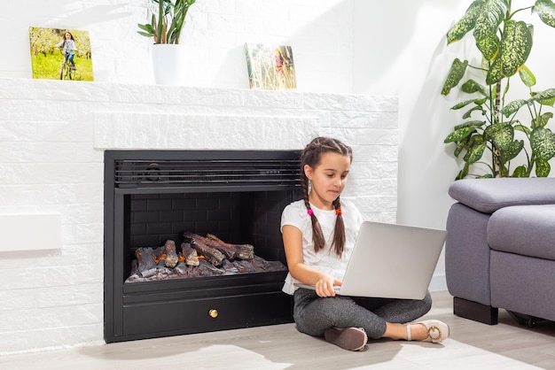 Foto van een positief meisje dat een laptop voor gebruik op afstand studeert, online communicatieles heeft met een tutor die binnenshuis een rapport schrijft