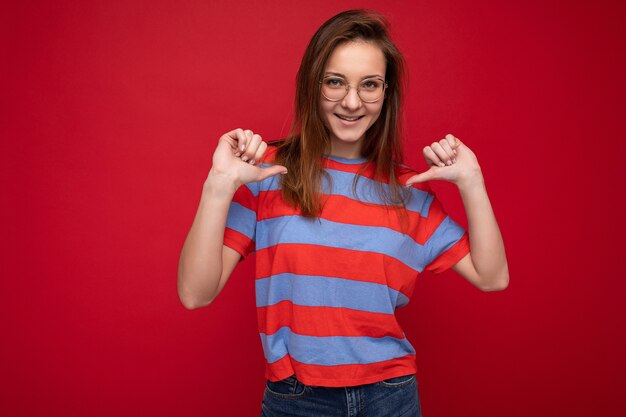 Foto van een positieve, gelukkige jonge, mooie brunette vrouw met oprechte emoties die casual gestreepte kleding draagt