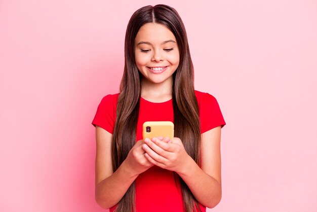 Foto van een positieve rode social media-post van een kindmeisje op een smartphone draagt een rood t-shirt geïsoleerd op een pastelkleurige achtergrond