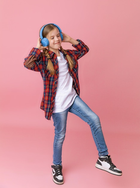 Foto van een schattige grappige jonge tienermeisje in een roze trui koptelefoon dansen genieten van muziek op een achtergrond